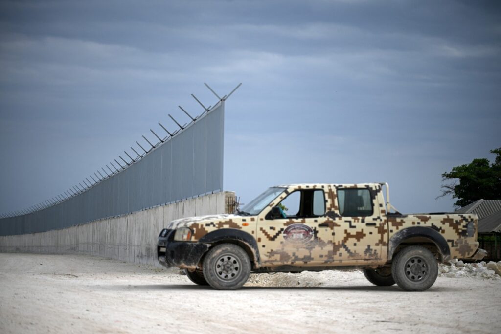 View of a patrol car parked next to the border wall being built in the Dominican Republic-Haiti border, in Pedernales, Dominican Republic on May 15, 2024. - In an attempt to curb illegal migration, the Dominican government is constructing a "symbolic wall" along the 340-kilometer border between the Dominican Republic and Haiti, covering 160 kilometers and starting in Pedernales, the least populated coastal province. (Photo by Federico PARRA / AFP)